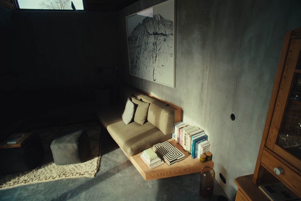Olive-green seating nook with a wooden shelf, exposed-concrete walls and floor